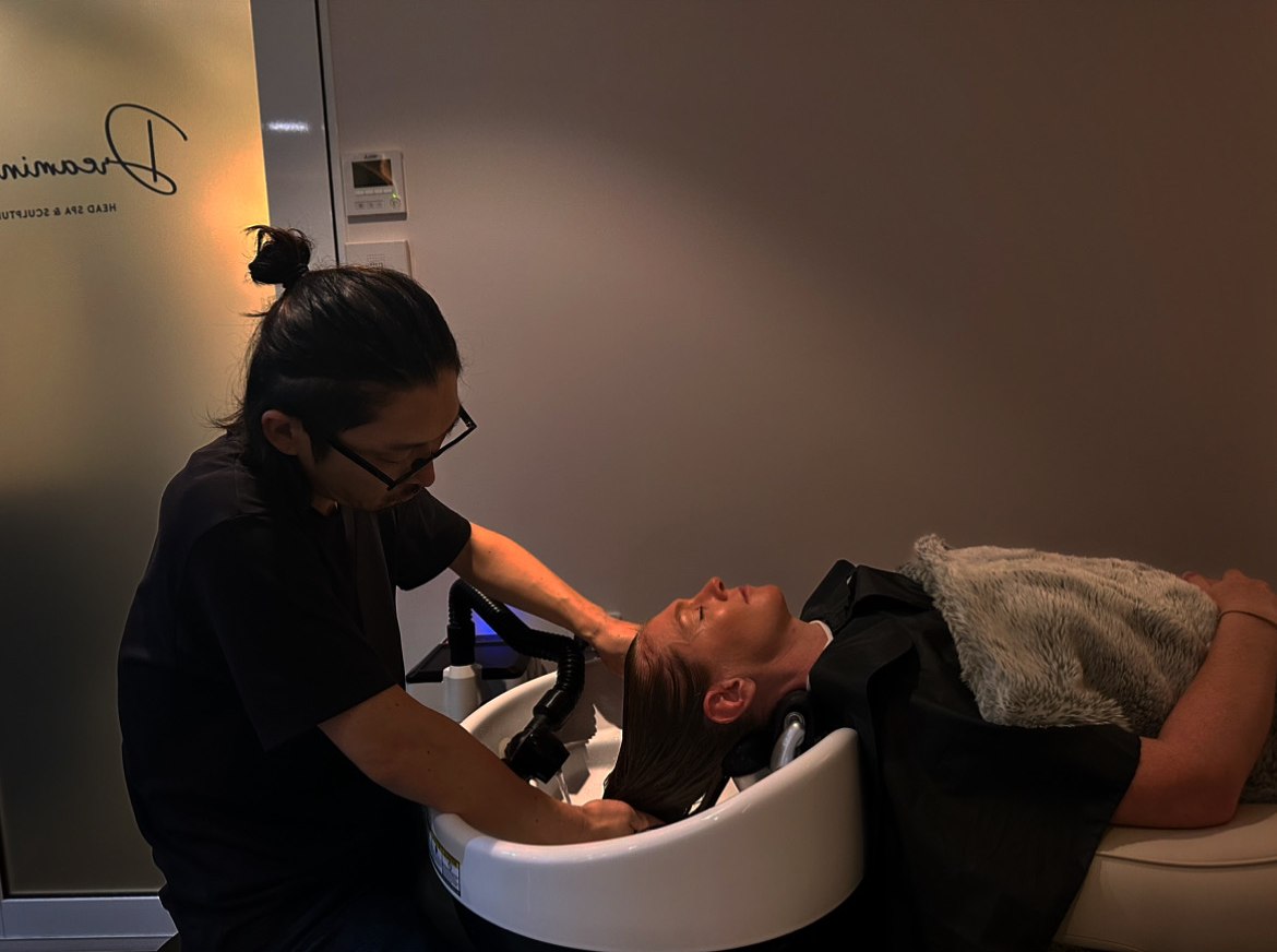 Takashi performing a wet head spa at Dreamin' — a guest lying fully flat as their scalp is treated at the basin