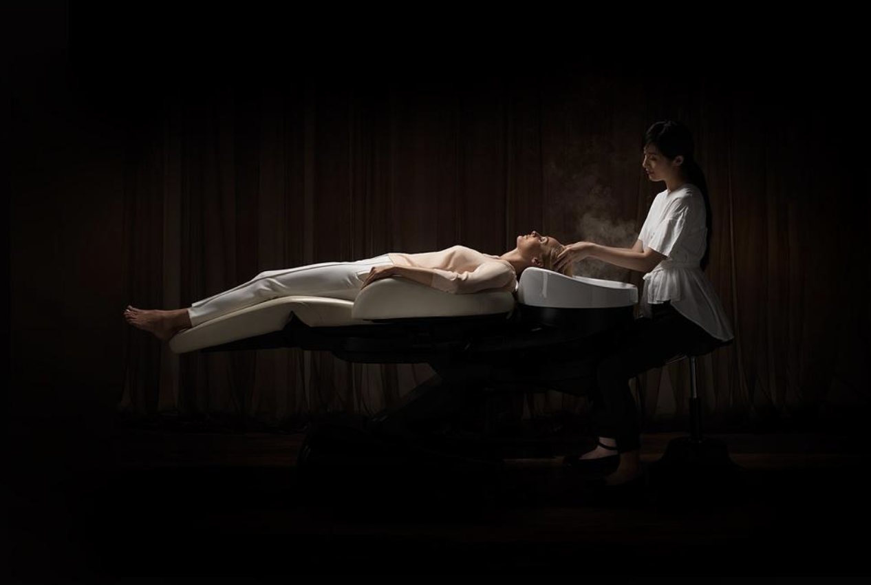 A head spa treatment underway on the flat shampoo bed in a darkened room