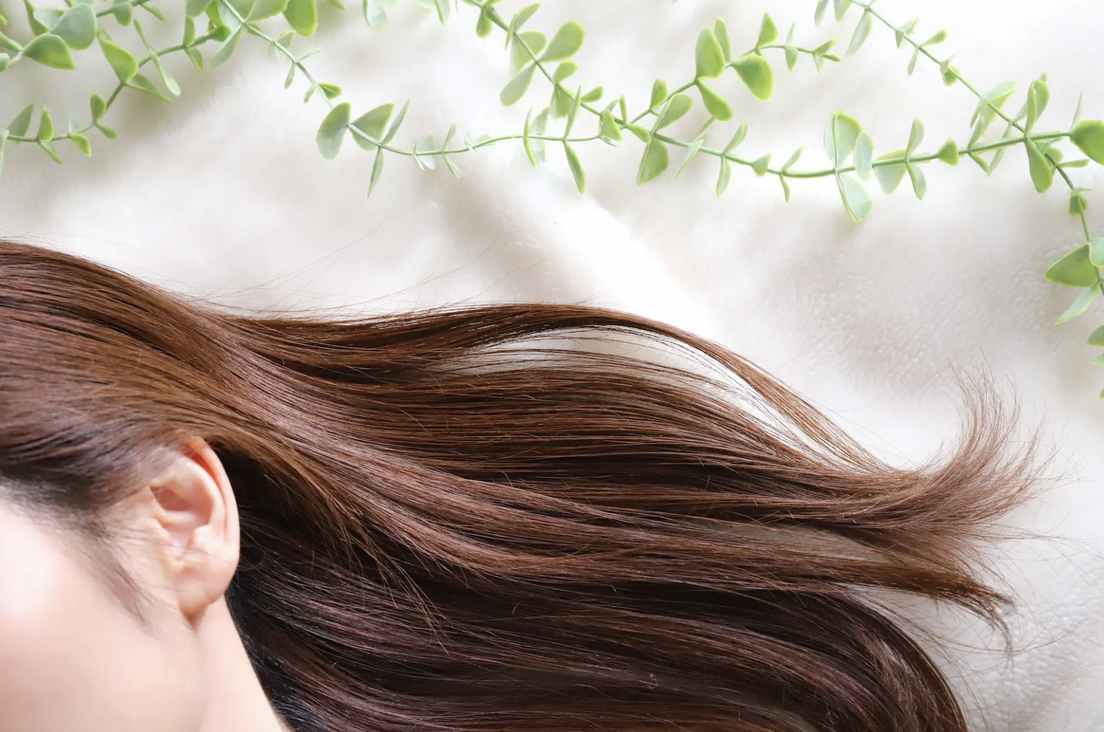 Hair spread across white bedding beneath trailing greenery
